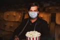 Portrait of a man wearing an anti-Covid-19 massager into the movie with popcorn.