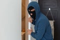 Portrait of man wearing blue hoodie and black robber mask, breaking flat, opening door, looking at camera, illegal cone in to