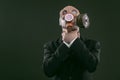 Portrait of a man wearing a business suit and an old gas mask while choking himself, isolated on dark green background