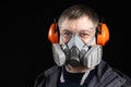 Portrait of a man wearing a respirator and protective noise-cancelling headphones earmuffs Royalty Free Stock Photo