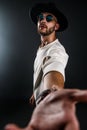 Portrait of a man in a wide-brimmed hat and sunglasses looking at camera while taking selfie on dark background. Royalty Free Stock Photo