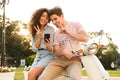 Portrait of man and woman wearing earphones smiling at smartphone while sitting on scooter together on city Royalty Free Stock Photo