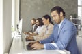 Portrait of man working on laptop sitting in row at desk with colleagues in modern office. Royalty Free Stock Photo