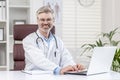 Portrait of a mature adult gray-haired doctor inside a medical office, the doctor is smiling and looking at the camera Royalty Free Stock Photo
