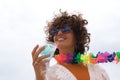 Portrait of mature, attractive woman, curly hair, with sunglasses, flower necklace and bikini, with a glass of blue wine in her Royalty Free Stock Photo