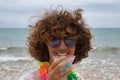 Portrait of mature, attractive woman with sunglasses and flower necklace drinking from a glass of blue wine on the beach. Concept Royalty Free Stock Photo