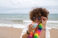 Portrait of mature, attractive woman with sunglasses, flower necklace and bikini, lowering her glasses with a glass of blue wine Royalty Free Stock Photo