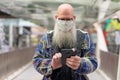 Mature bald bearded man with mask using phone in the city Royalty Free Stock Photo