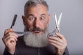 Portrait of mature bearded man with retro razor and scissors, barbershop concept, selective focus