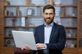 Portrait of mature businessman inside office, senior man in business suit and beard standing and holding laptop, boss at Royalty Free Stock Photo