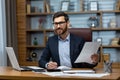 Portrait of mature businessman inside office at workplace, man with documents smiling and looking at camera, paperwork