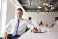 Portrait Of Mature Businessman Sitting In Modern Boardroom With Colleagues Meeting Around Table In Background Royalty Free Stock Photo