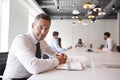 Portrait Of Mature Businessman Sitting In Modern Boardroom With Colleagues Meeting Around Table In Background Royalty Free Stock Photo