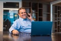 Portrait of mature businessman using laptop computer in office and talking on mobile phone Royalty Free Stock Photo