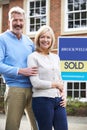 Portrait Of Mature Couple Standing Outside Dream Home Wit Sold Sign