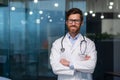 Portrait of mature doctor with beard, man in white medical coat smiling and looking at camera with crossed arms working Royalty Free Stock Photo
