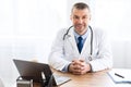 Portrait of mature doctor looking at camera sitting at desk Royalty Free Stock Photo