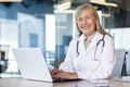 Portrait of mature experienced female doctor, gray-haired senior woman in white medical coat smiling looking at camera Royalty Free Stock Photo