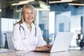 Portrait of mature experienced female doctor, gray-haired senior woman in white medical coat smiling looking at camera Royalty Free Stock Photo