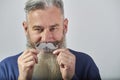 Portrait of mature gray-haired bearded man in blue sweatshirt with mustache comb on gray background, selective focus