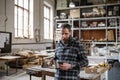 Portrait of mature male carpenter with coffee and smrtphone indoors in carpentery workshop.