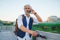 Portrait of mature man with electric scooter outdoors in city, using smartphone. Royalty Free Stock Photo