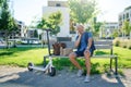 Portrait of mature man with electric scooter sitting outdoors in city, using smartphone. Royalty Free Stock Photo