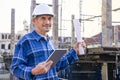 portrait mature man engineer in checkered shirt wears safety helmet, one hand holding tablet and other hand holding blueprint Royalty Free Stock Photo