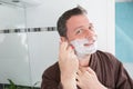 mature man in front of mirror applying facial cream is ready to shave