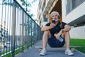 Portrait of mature man with headphones sitting outdoors in city, using smartphone. Royalty Free Stock Photo