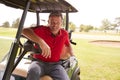 Portrait Of Mature Man Playing Golf Driving Buggy Along Course To Green On Red Letter Day