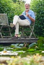 Portrait Of Mature Man Relaxing In Garden Reading Book On Jetty By Lake Royalty Free Stock Photo