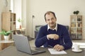 Portrait of mature man sitting at desk with laptop computer looking at camera Royalty Free Stock Photo