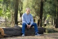 portrait mature man spend leisure time sitting on a log in the forest park Royalty Free Stock Photo