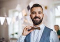 A portrait of a mature man standing indoors on a party, holding wooden bowtie.