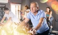 Portrait of mature man taking indoor cycling class at fitness center, doing cardio riding bike Royalty Free Stock Photo