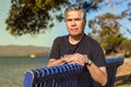 Portrait of a mature man 57 years with gray hair looking camera sitting on a bench at a beach outdoors, confident Royalty Free Stock Photo