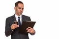 Portrait of mature Persian businessman using phone while reading on clipboard Royalty Free Stock Photo
