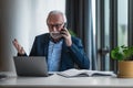 Portrait of mature senior businessman entrepreneur in casual business office making phone call and gesturing while working with Royalty Free Stock Photo