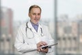 Portrait of mature senior male doctor holding digital tablet standing indoors. Royalty Free Stock Photo