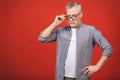 Portrait of a mature serious businessman with crossed hands wearing glasses isolated against red background. Senior man looking at Royalty Free Stock Photo