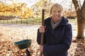 Portrait Of Mature Woman Raking Autumn Leaves In Garden