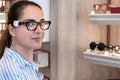 Portrait of a mature woman shopping, standing in store and trying eyeglasses frame, looking camera Royalty Free Stock Photo