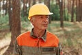 Portrait of mature woodsman posing in forest in open air and looking away with pensive expression, wearing uniform and yellow