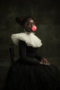 Portrait of medieval African young woman in black vintage dress with big white collar posing isolated on dark green