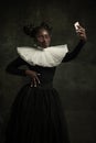 Portrait of medieval African young woman in black vintage dress with big white collar posing isolated on dark green