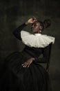 Portrait of medieval African young woman in black vintage dress with big white collar posing isolated on dark green