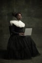 Portrait of medieval African young woman in black vintage dress with big white collar posing isolated on dark green