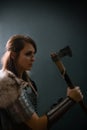 Portrait of a medieval fantasy female warrior in armor armed with an ax, posing in the studio in the dark on a black background