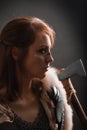 Portrait of a medieval fantasy female warrior in armor armed with an ax, posing in the studio in the dark on a black background